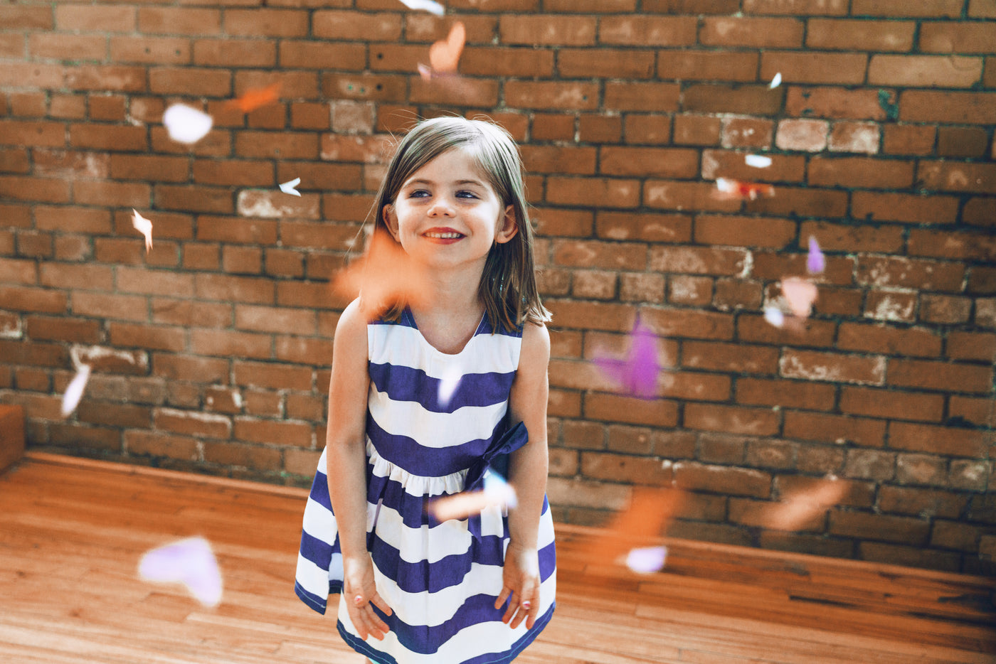 Child in a blue and white striped dress playing among falling paper confetti