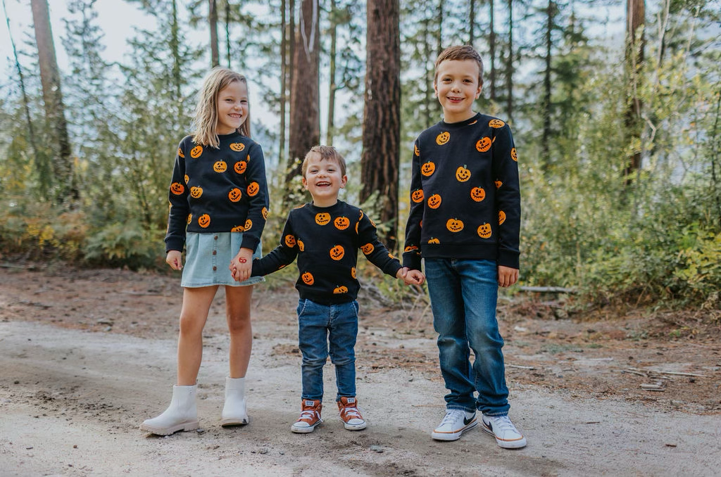 Three children wearing pumpkin-print tops outdoors